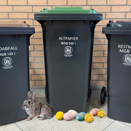 Hase und Ostereier vor drei Mülltonnen