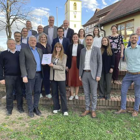 Die Bürgermeister der 11 ILE-Gemeinden der „Baunach-Allianz“ mit den Vertretern der Planer und Behörden mit Vorsitzenden Jürgen Hennemann (vordere Reihe 2. von links), der von Jennifer Gannek die „ILEK-Fortschreibung“ erhält, sowie Umsetzungsbegleiter Felix Henneberger (vordere Reihe rechts).